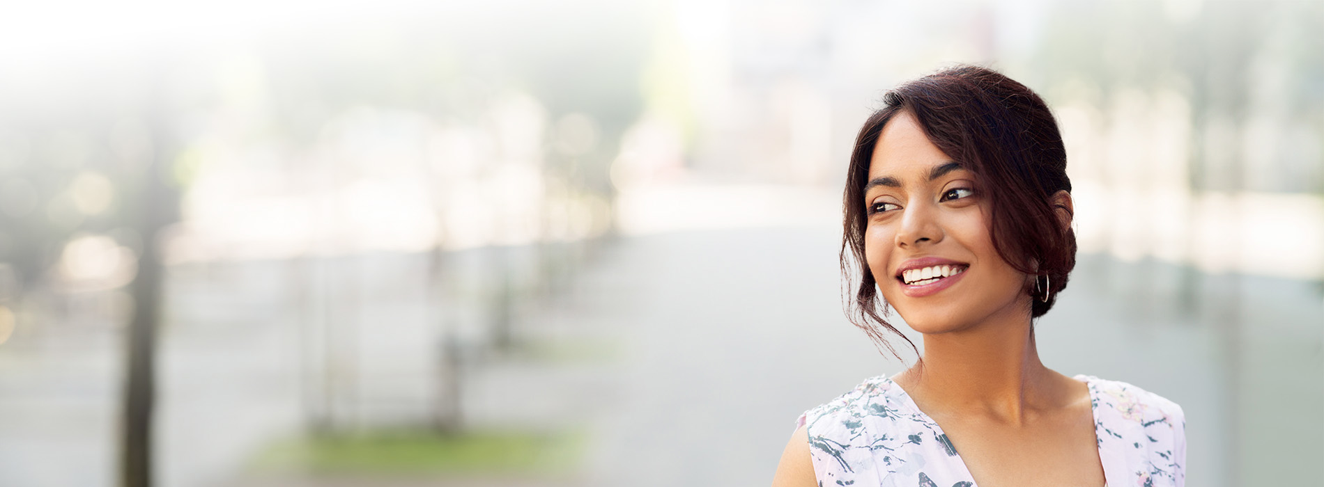 A woman with short hair smiles at the camera, wearing a sleeveless top, against a blurred background.