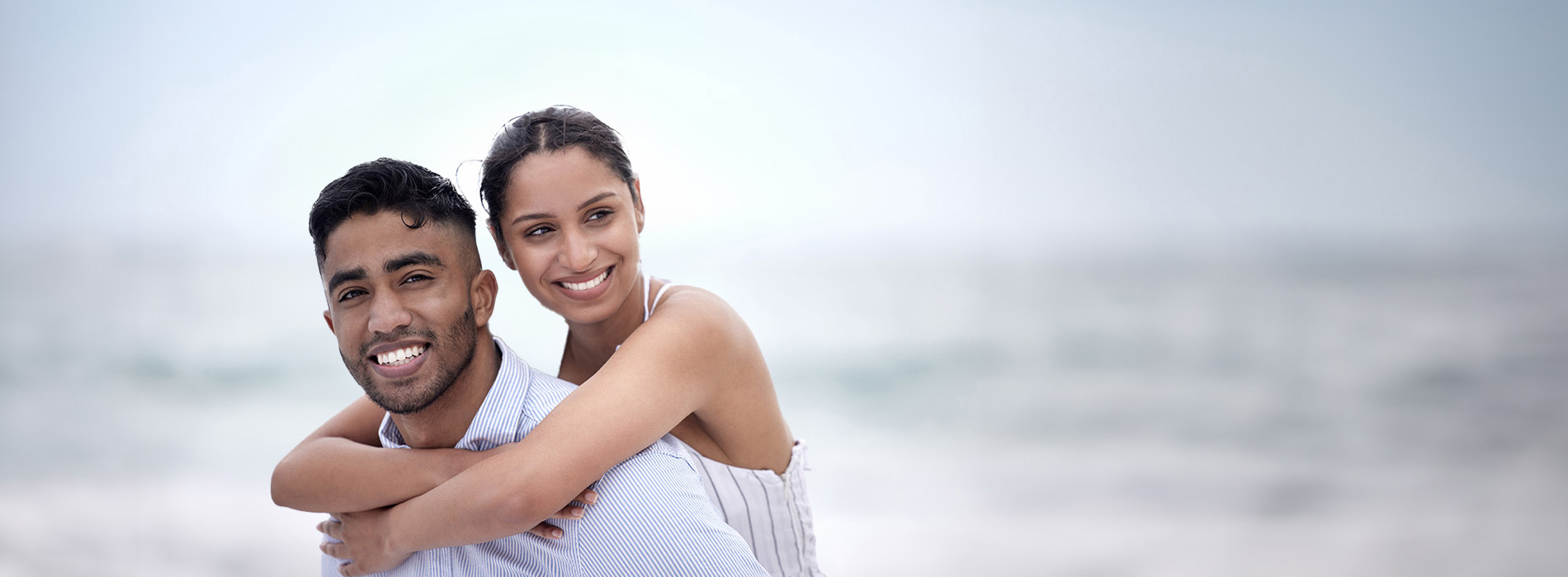 The image features two people embracing each other on a beach, with clear skies and calm waters visible in the background.