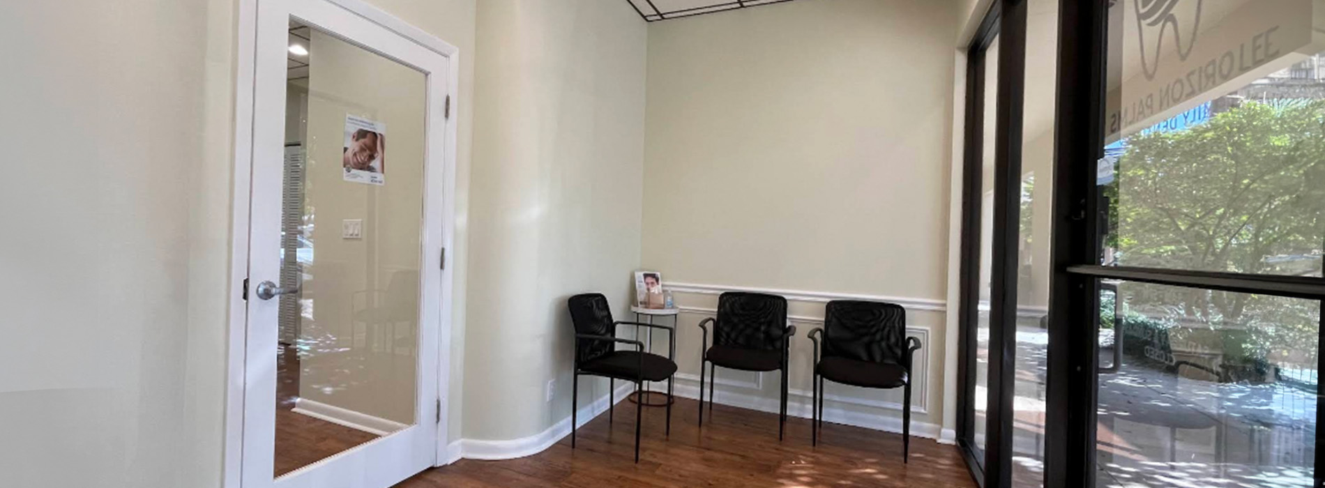 The image shows an interior view of a room with a clean and modern design, featuring a reception area with chairs, a desk, and a window, set against a wall with a large mirror reflecting the space.
