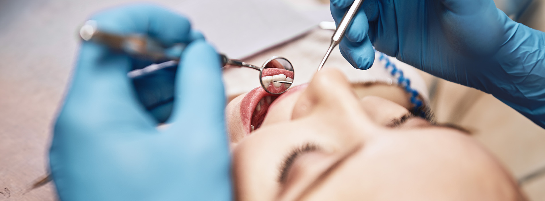 The image shows a person receiving dental care, with a dental professional working on their teeth using tools visible in the frame.