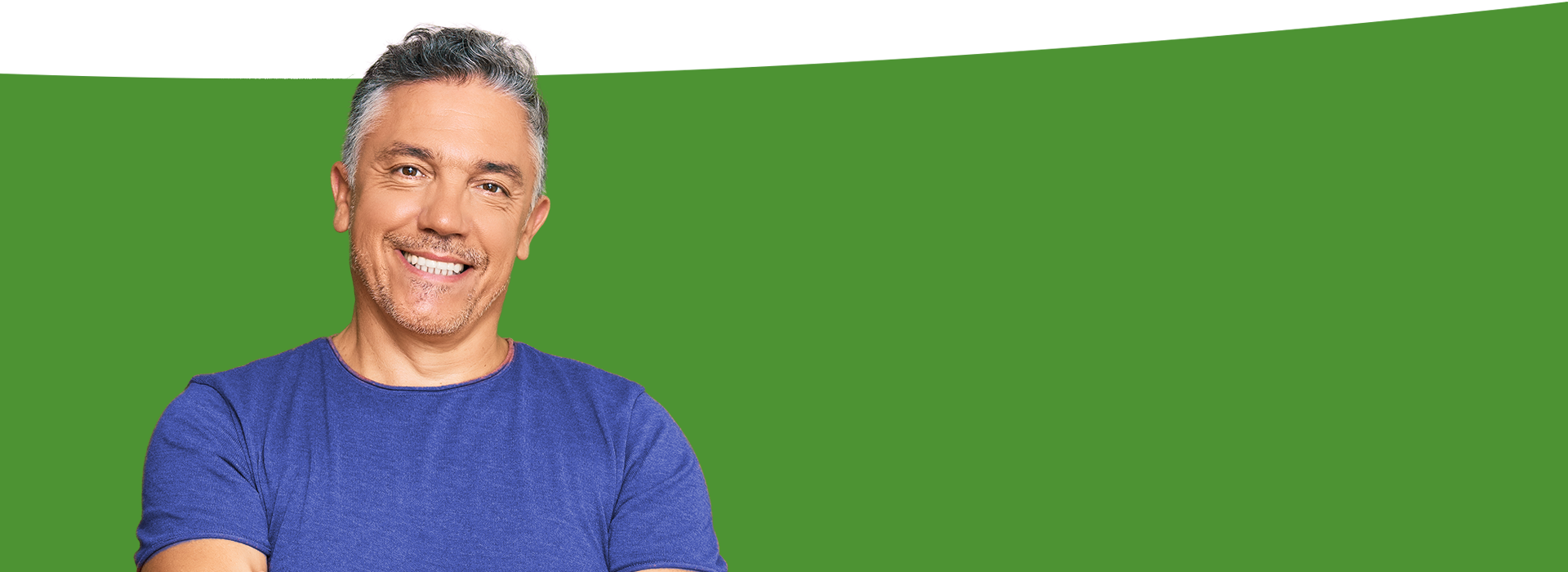 The image shows a man with a beard smiling at the camera, wearing a blue shirt, standing against a green background with a white stripe.