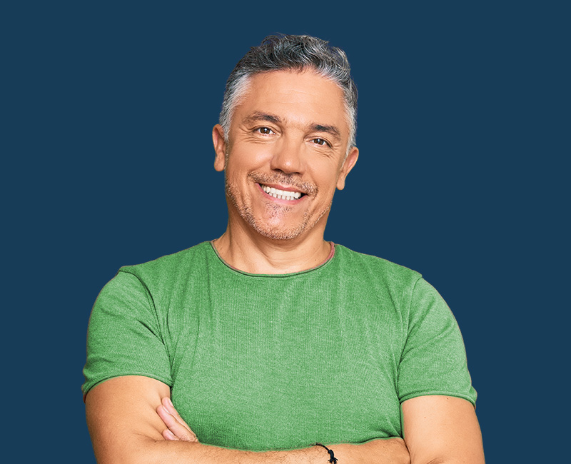 The image shows a man standing confidently with his arms crossed, wearing a green t-shirt, smiling at the camera.