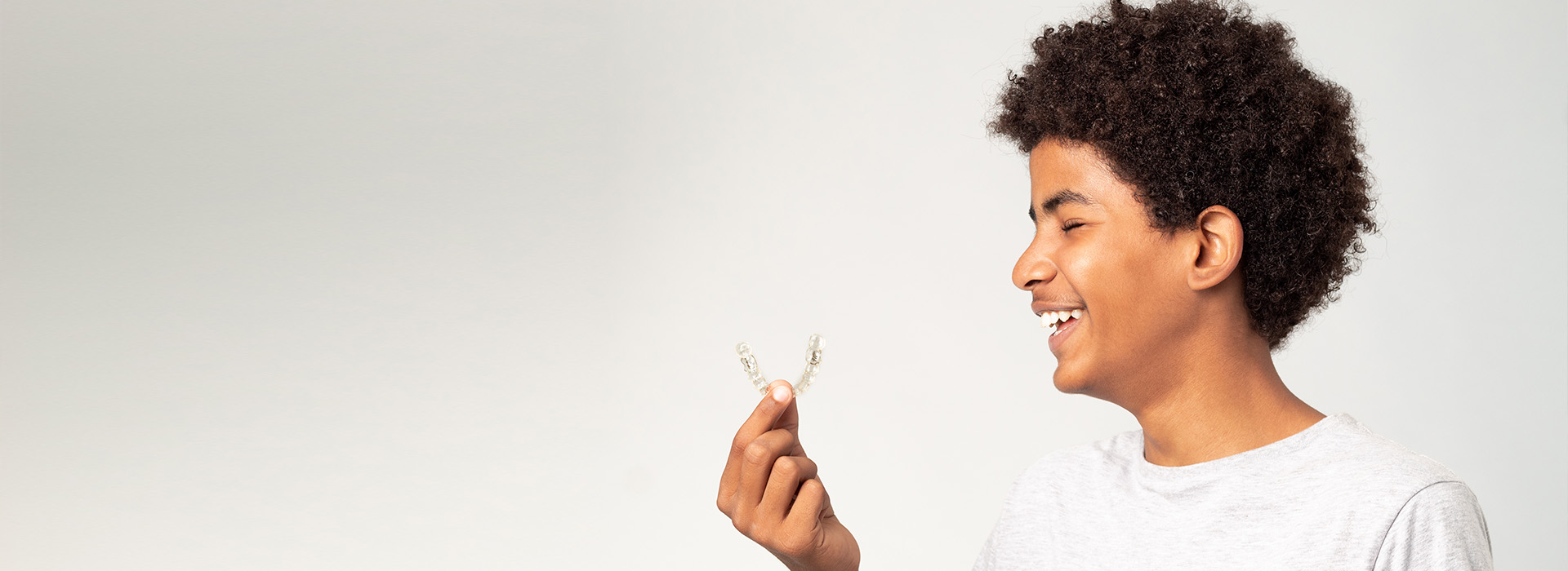 The image shows a person with curly hair holding a small object near their face, smiling, against a plain background.