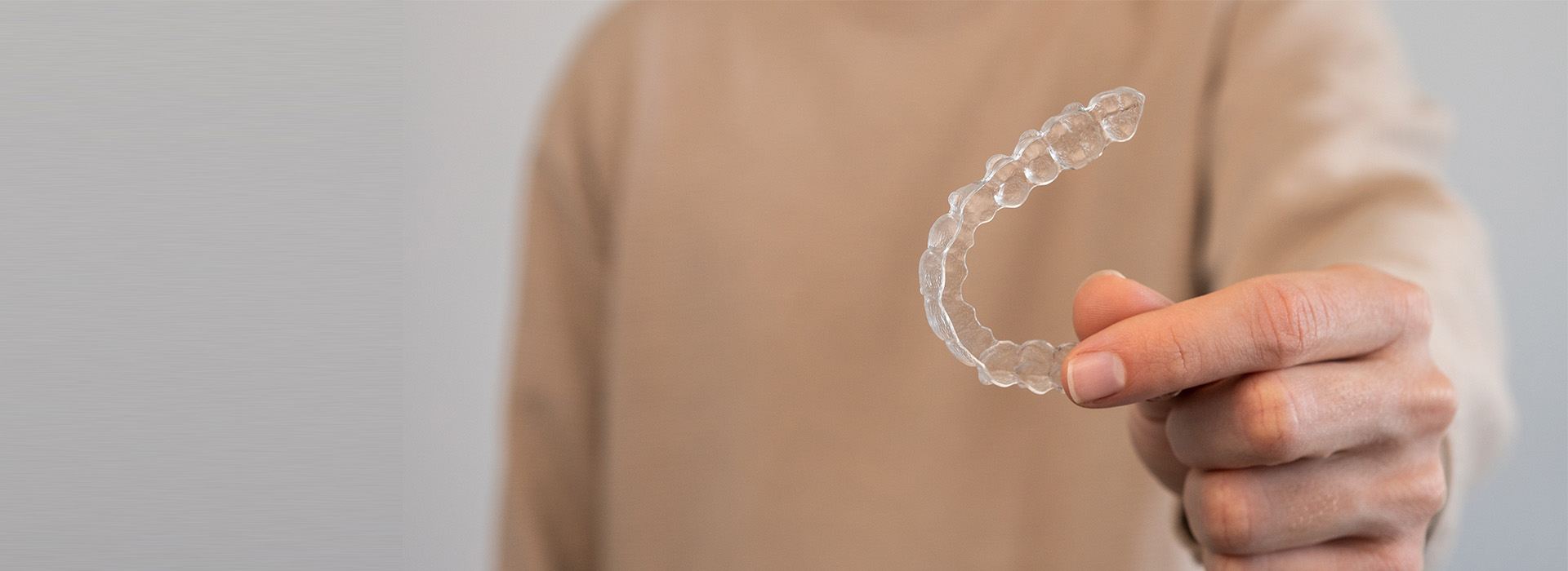 The image shows a person holding a clear plastic ring with their hand, against a blurred background.