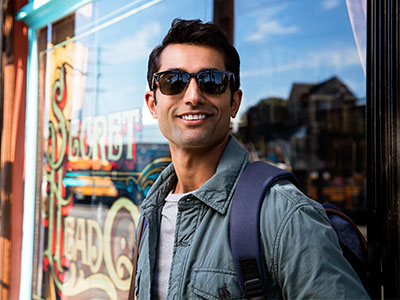 In the image, a man wearing sunglasses and a backpack stands confidently outside a storefront with a sign that reads Sweet Treats.