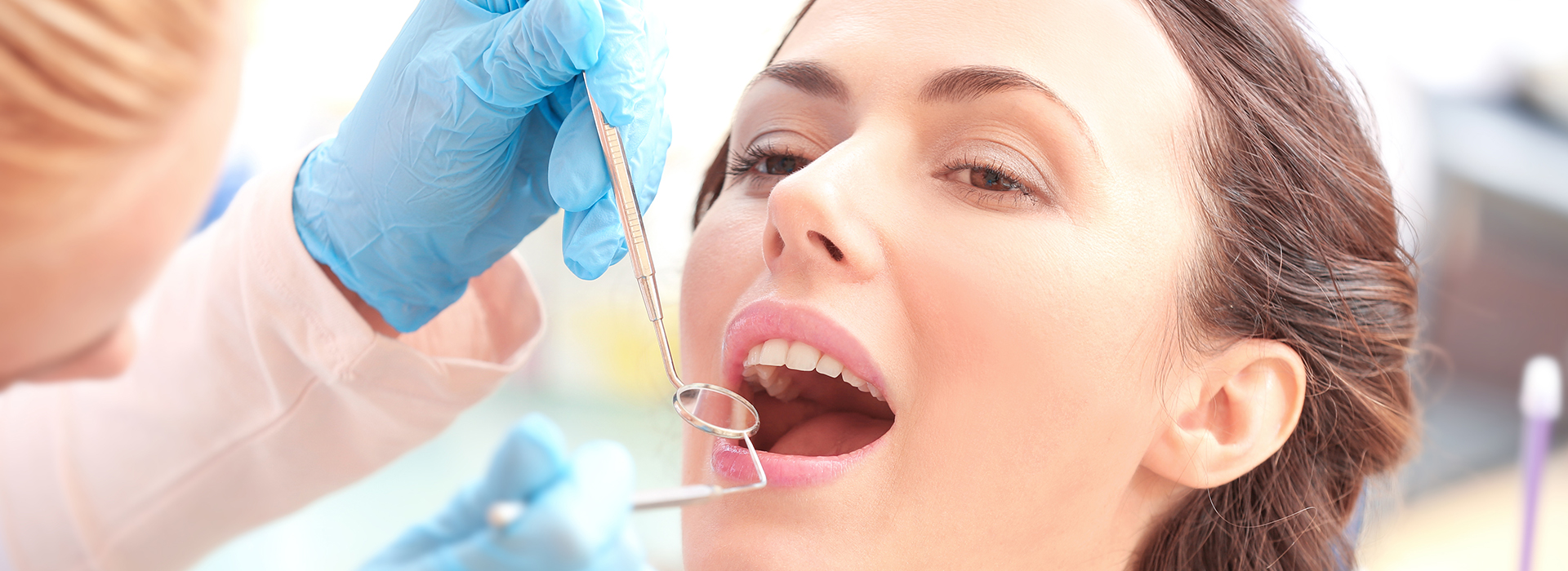 The image shows a woman receiving dental treatment, with her mouth open and a dentist working on her teeth using dental tools.