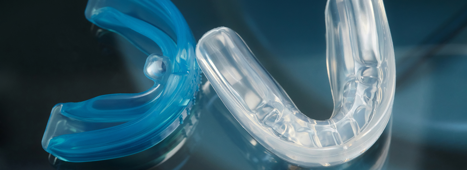 The image shows a close-up of a blue plastic object with a clear transparent center, resembling a toothbrush head, positioned against a dark background.