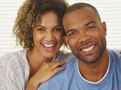 A man and woman pose together with smiles, sharing a close moment.