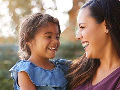 The image shows a woman holding a young child with a smile on her face, suggesting a joyful moment between them.