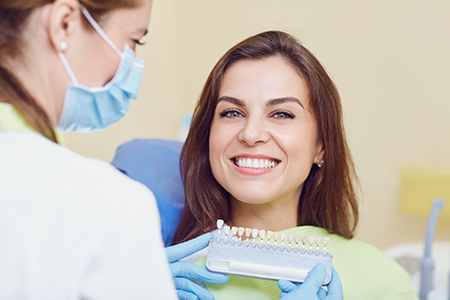 A smiling woman receiving dental care from a dentist, with the dental professional holding a device near her mouth.