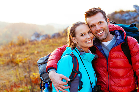 A man and woman are embracing each other in a field with backpacks, smiling at the camera.