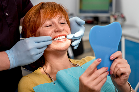 Woman sitting in dental chair with blue mouthguard, smiling at camera, surrounded by dental professionals performing oral care.