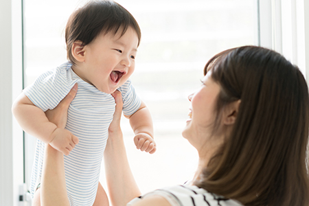 A woman holding a baby with an open mouth, possibly laughing or singing, appears joyful while looking at the camera.