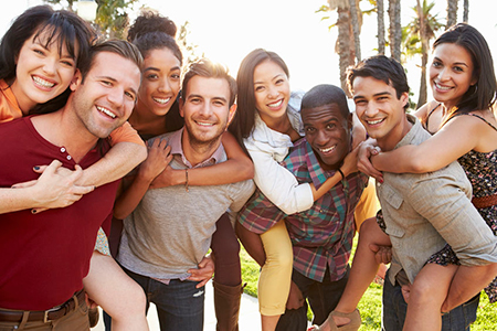 A group of young adults posing together outdoors with smiles on their faces, some hugging each other.