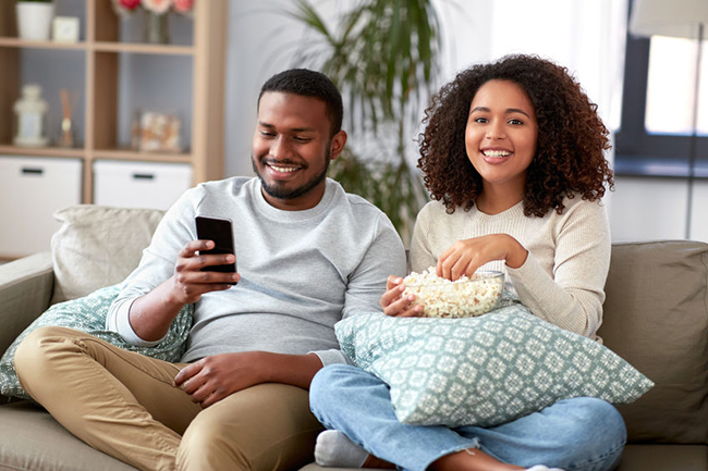 A young couple sitting on a couch together, engaged with each other and a cell phone, enjoying a moment of relaxation at home.