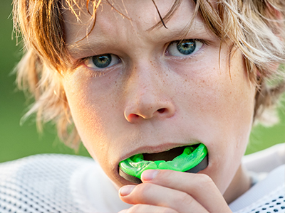 A split-screen photo showing a young boy with blonde hair and blue eyes on the left, holding a football gum, and a close-up of the same boy on the right, with a look of disgust or disapproval while holding the gum in his mouth.